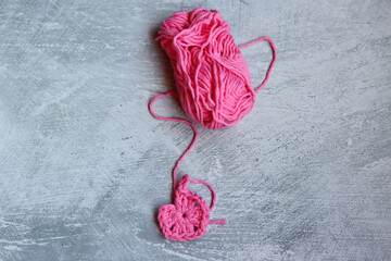 Soft cotton yarn, crochet hook and crochet project in process on grey stone background. Top view...