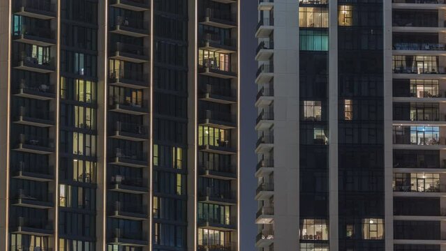 Tall blocks of flats with glowing windows located in residential district of city aerial timelapse. Evening light in apartments in towers and skyscrapers