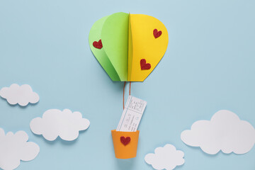 Paper hot air balloon with ticket and clouds on blue background. Valentine's Day celebration