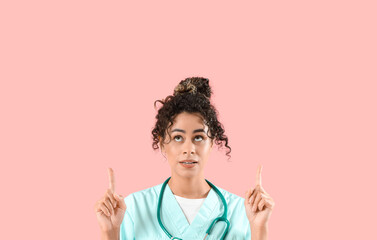 Female African-American medical intern with stethoscope pointing at something on pink background