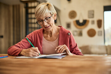 A senior woman, holding and using a crayon, coloring the coloring book.