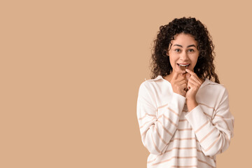 Fototapeta na wymiar Beautiful young African-American woman eating piece of sweet chocolate on brown background