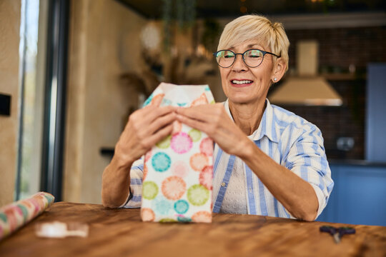 A happy senior woman packing a gift for someone, using decorative wrapping paper.