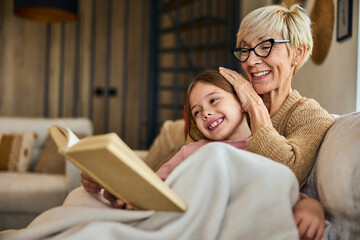 Grandma and grandchild spending time together, covered in a blanket, reading a book together.