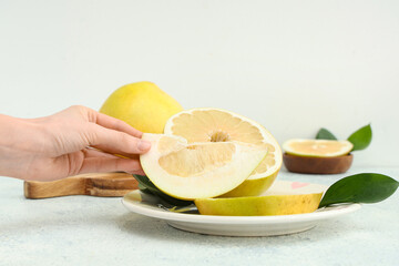 Female hand with plate of cut fresh pomelo fruit on white background