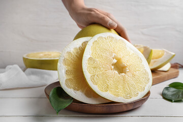 Female hand with board of fresh pomelo fruits on white wooden table