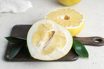 Wooden board with halves of fresh pomelo fruit and leaves on white background