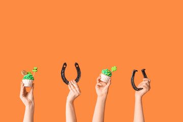 Female hands with tasty cupcakes and horseshoes for St. Patrick's Day on orange background