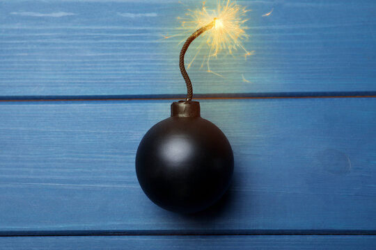 Old fashioned black bomb with lit fuse on blue wooden table, top view