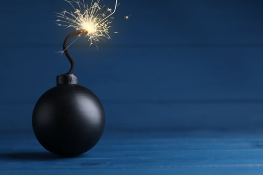 Old fashioned black bomb with lit fuse on blue wooden table, space for text