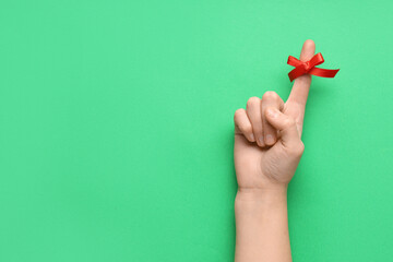 Female hand with red bow on index finger against green background. Reminder concept