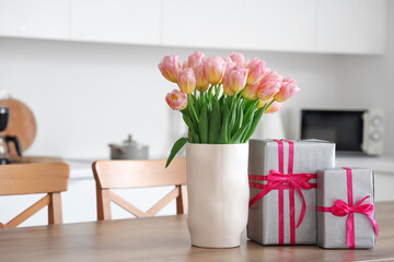 Vase with tulips and gift boxes for International Women's Day on table in kitchen