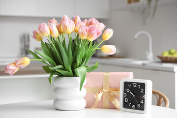 Vase with tulips, gift box for International Women's Day and clock on table in kitchen