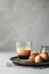 egg liquor and coffee cocktail in glass and beige eggs on the light grey background, copy space