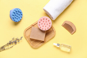 Hair scalp massagers with shampoo bar and cosmetic oil on yellow background