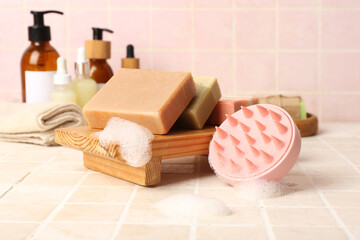 Hair scalp massager with shampoo bars and bottles of cosmetic products on pink tile background
