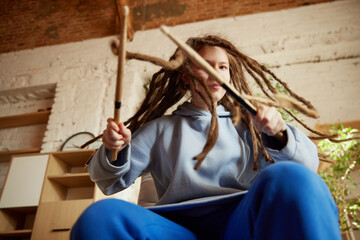 View from below. Youthful drummer, girl with dreadlocks practicing with drumsticks in casual attire...