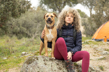 Curly hair and mountaineer woman and her dog posing outdoor during his walk through the mountains.