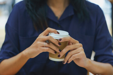 Close-up hand of Asian businesswoman holding a delivery cup of coffee.