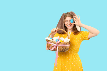 Beautiful young happy woman in bunny ears with Easter basket and painted eggs on blue background