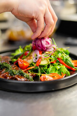 chef hand cooking Roast beef salad with vegetables on restaurant kitchen