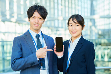 スマートフォンの画面を見せるスーツ姿の男女