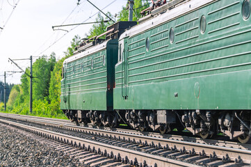 A green electric train is moving along the railway tracks. Delivery of goods by rail. The wagons...