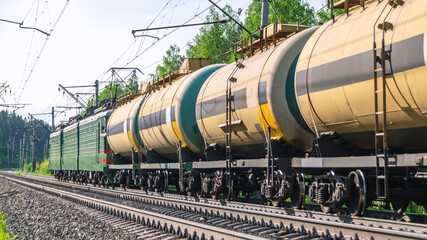 Fototapeta na wymiar The train is moving along the railway tracks. The tank car is pulled by two locomotives. Transportation of petroleum products by rail. Tanks with flammable chemical liquids. Cars with liquefied gas.