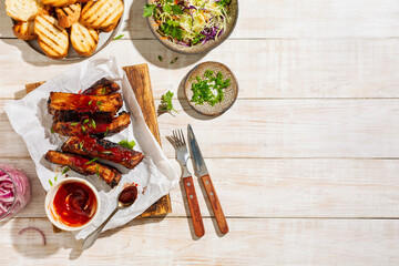 Grilled and smoked ribs with barbeque sauce on a carving board served with coleslaw salad and green onions. Top view, wooden background.