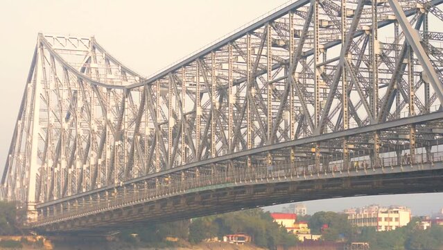 9th February, 2024, Kolkata, West Bengal, India: Beautiful landscape of a fishing boat on River Ganges crossing Howrah Bridge at the time of sunrise.
