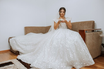 An incredibly beautiful bride sits on a bed in her bedroom. Bride morning. A gorgeous bride in a...