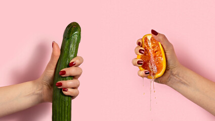 Female hand with half of juicy orange and cucumber on pink background. Sex concept.