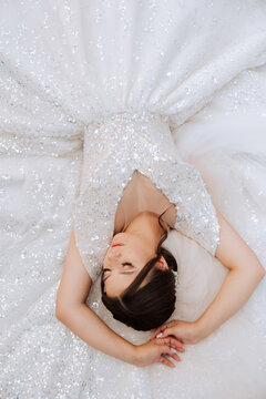 A brunette bride is lying on a lace dress, posing with closed eyes