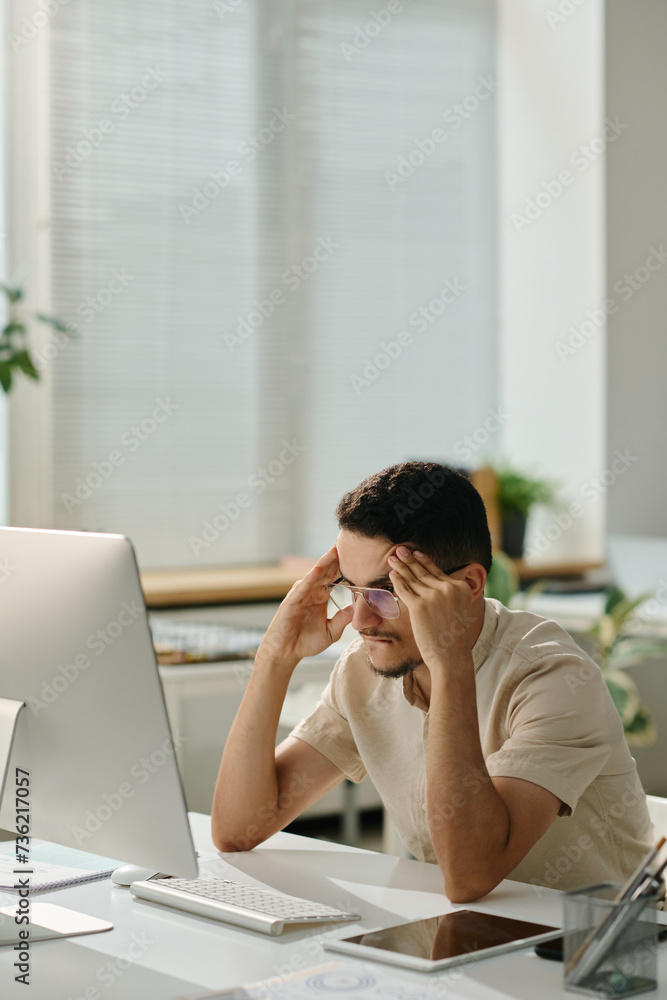 Poster anxious male office worker trying to concentrate while sitting in front of computer screen and looki