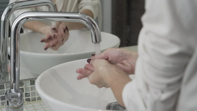 Closeup of a woman washing her hands with liquid soap suds in the bathroom sink. Hand hygiene from bacteria. Foam foams in women's hands