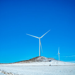 Wind turbine generating electricity between an snowy field and a blue sky background for copy space. - 736223832