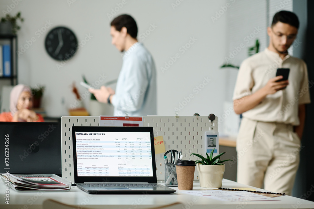 Aufkleber Laptop with summary of results on screen standing on desk which is workplace of analyst or broker against young employees