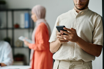 Cropped shot of young Muslim businessman in casualwear standing in front of camera and texting in...