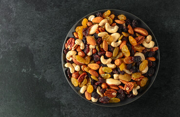 Mix of dried nuts and raisins on a black stone background.