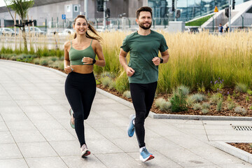 Active couple jogging together in urban park setting, promoting fitness. - obrazy, fototapety, plakaty