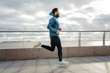 Solo male runner with intense focus running by the sea, symbolizing persistence.
