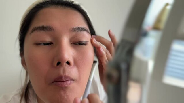 Asian woman in white t-shirt wearing make up in the living room.