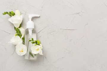 Cosmetic bottle with freesia flowers on concrete background, top view