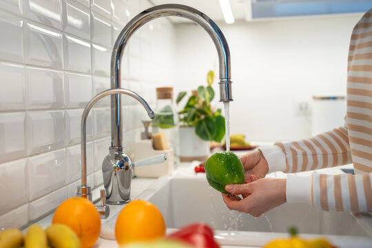 Healthy vegan food. Freshly delivered locally grown organic fruits and vegetables washing under water for vegetarian natural raw eating. Hands holding green paprika pepper on home kitchen. Detox diet. - Powered by Adobe