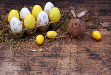 Osterhase mit gelben Ostereiern in einer Eierschachtel auf altem Holzbrett mit Platz für Text.