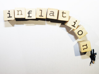 Inflation written with wood cubes. Small figurine wearing a suit standing on one letter signaling...