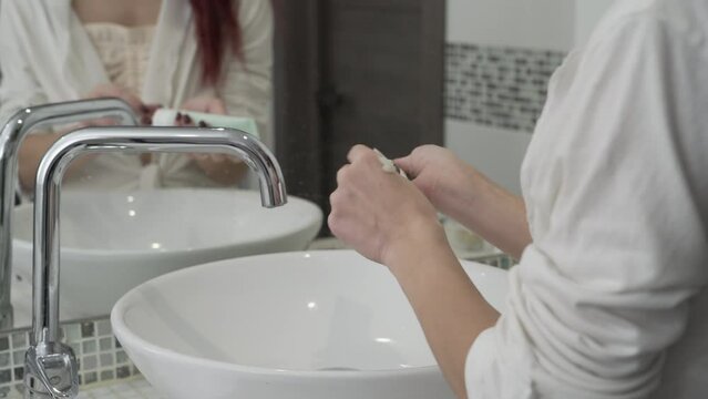 Young woman applies hand moisturizer to her hands for a softening effect in the bathroom. Body and skin care
