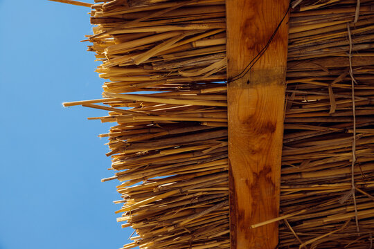 dry reed roof texture, thatched roof, palapa roof in blue sky. Wooden beach sun summer canopy. View from below