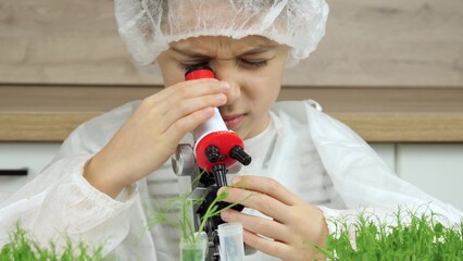 The kid looks into the microscope. A boy in a medical suit studies plants, microgreen shoots. Grass.