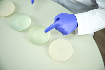 Close-up of female plastic surgeon demonstrates breast implants to a patient for her new breast. The plastic surgeon holds breast silicone implants. Breast augmentation concept. Breast Implant Samples